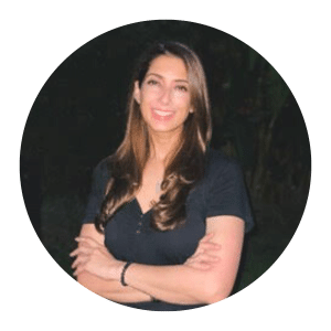Circular headshot of a smiling woman with long brown hair and arms crossed wearing a dark top
