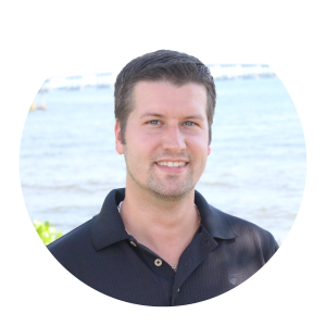 Circular headshot of a smiling man in a dark polo shirt with a waterfront background