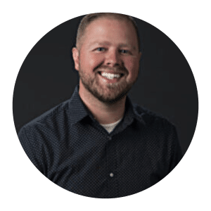Circular headshot of a smiling man with a beard wearing a dark button-up shirt