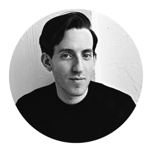 Black and white circular headshot of a man wearing a dark crew-neck top