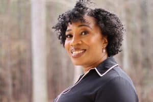 Professional headshot of a woman smiling outdoors in a dark collared top