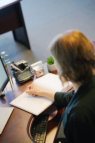 a woman at an office desk, writing in a notebook, deciding between life coach liability insurance