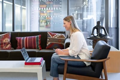 a woman in a glass walled office, siting on a chair in front of a laptop