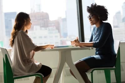 two women sitting at a table holding a conversation overlooking a cityscape