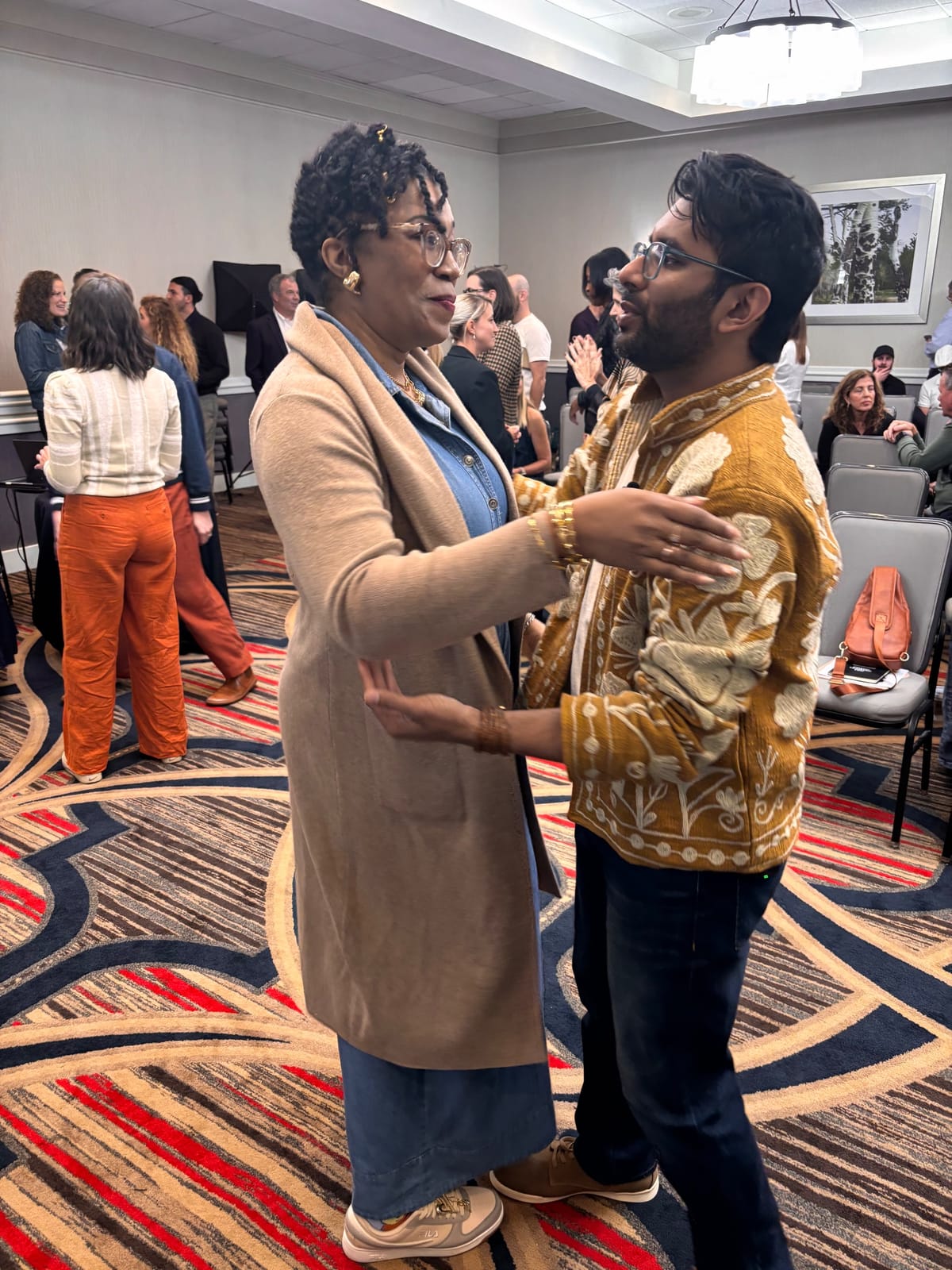 Two attendees greet each other with a warm embrace between sessions in the conference room