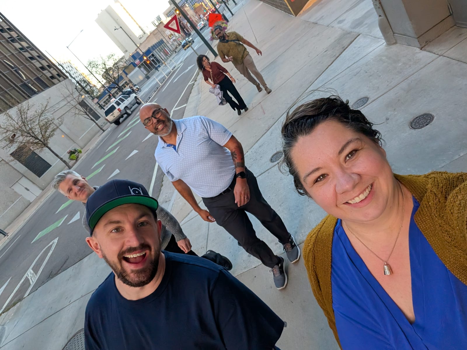 An attendee takes a selfie on a Denver street while fellow attendees walk behind in the sunset light